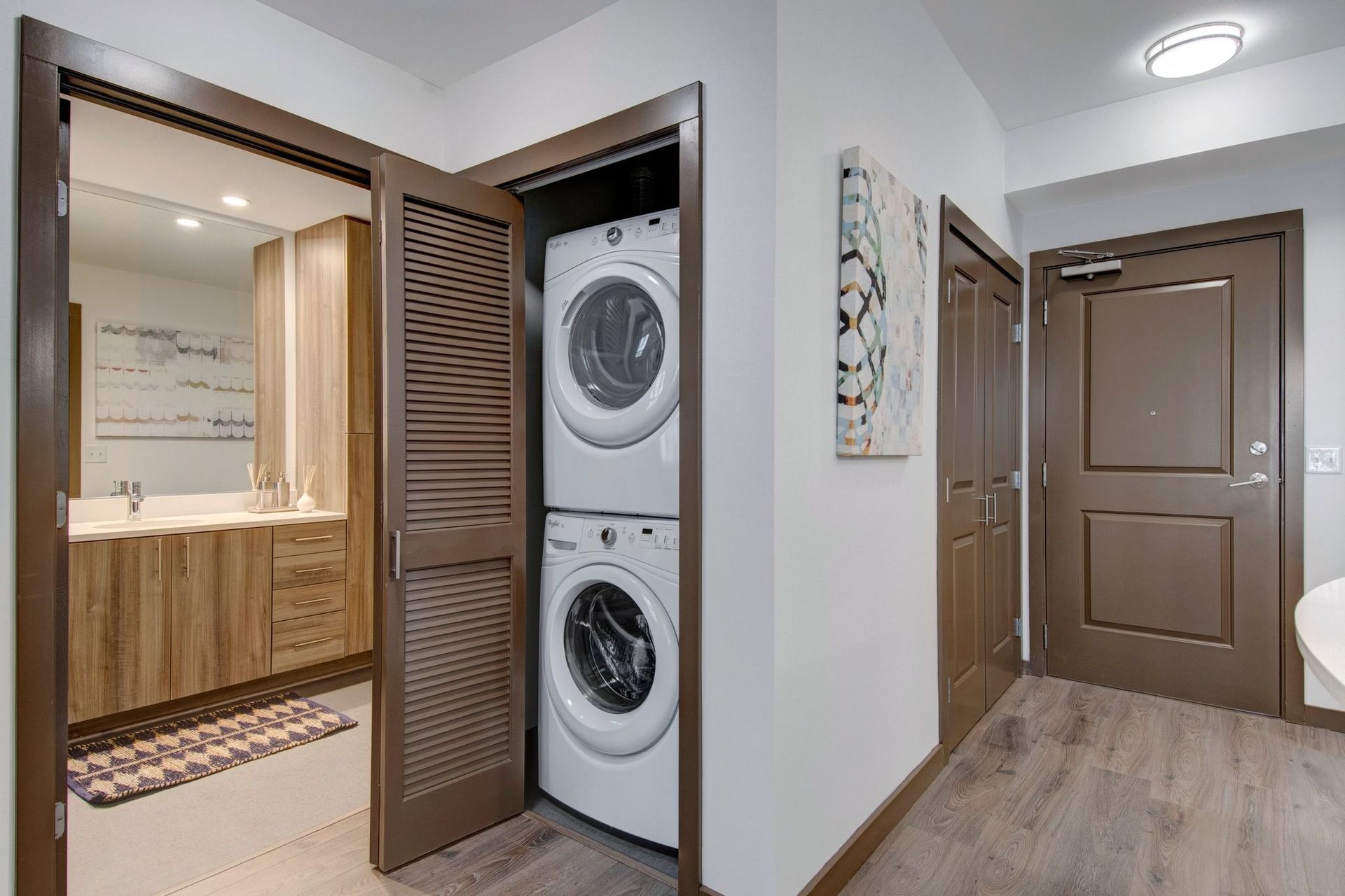 Interior hallway showing stacked washer and dryer in a closet next to a bathroom with wood vanity.