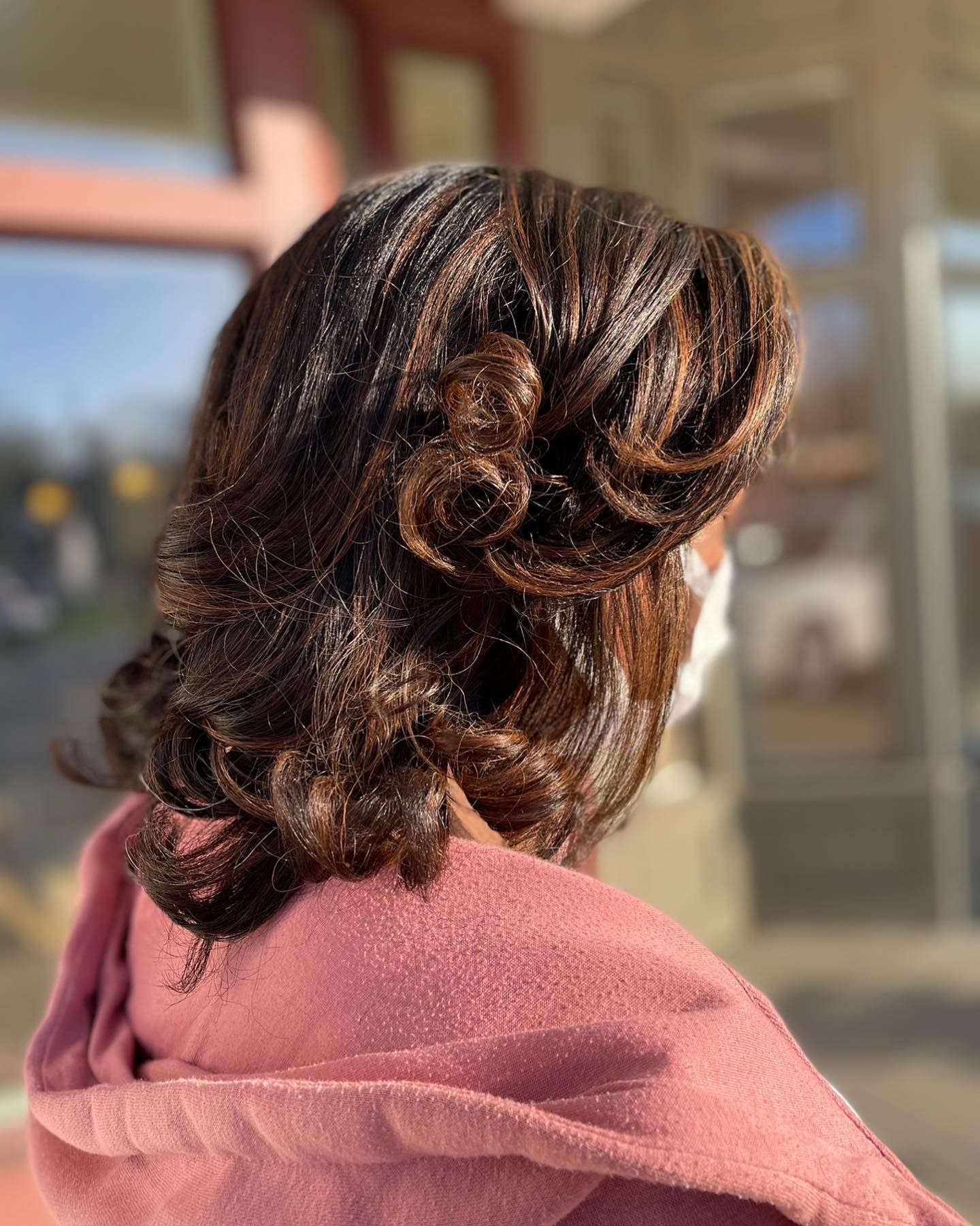 A woman wearing a mask and a pink scarf has her hair in a bun.