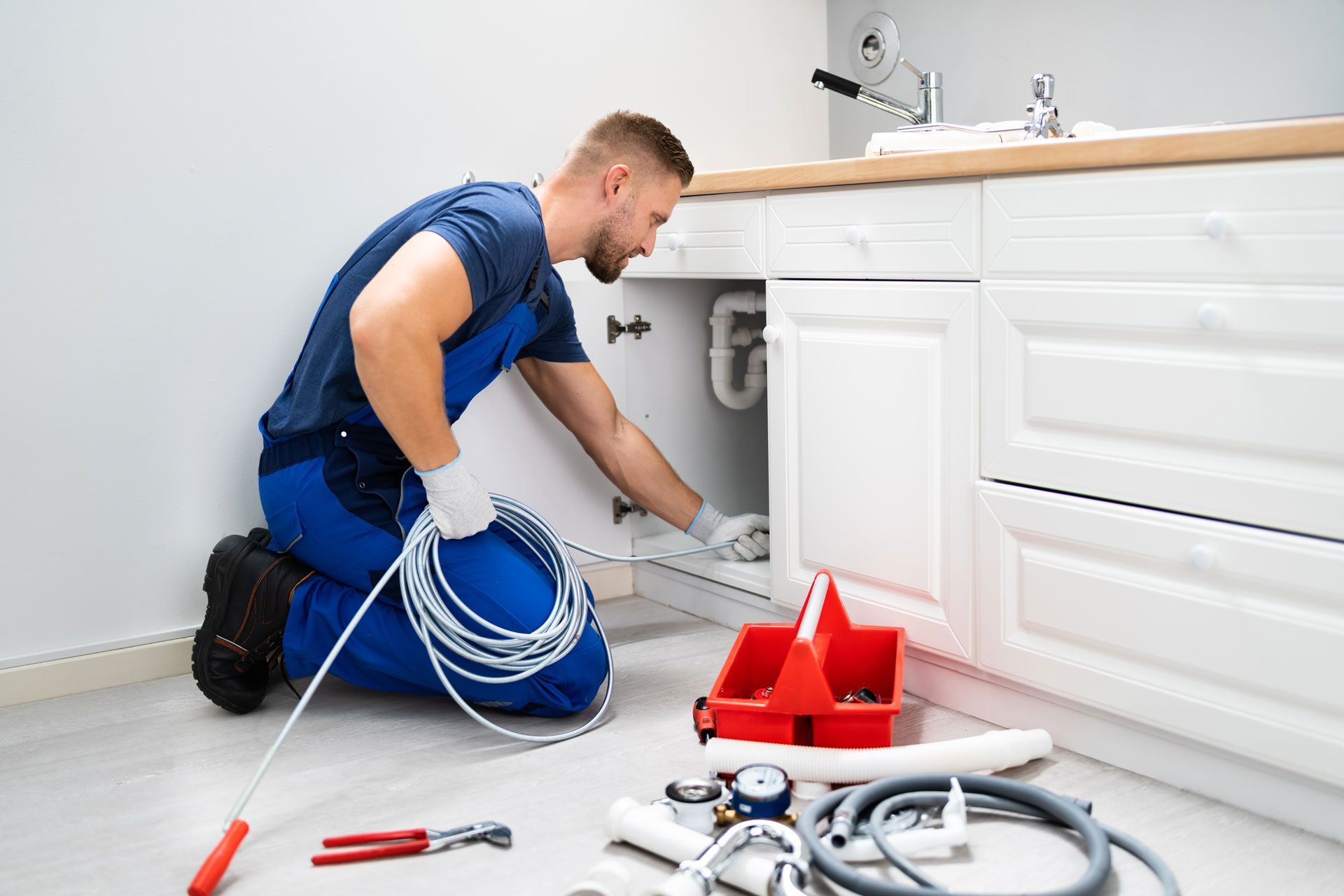 Plumber kneeling under a sink, fixing pipes with tools and coiled hoses on the bathroom floor.