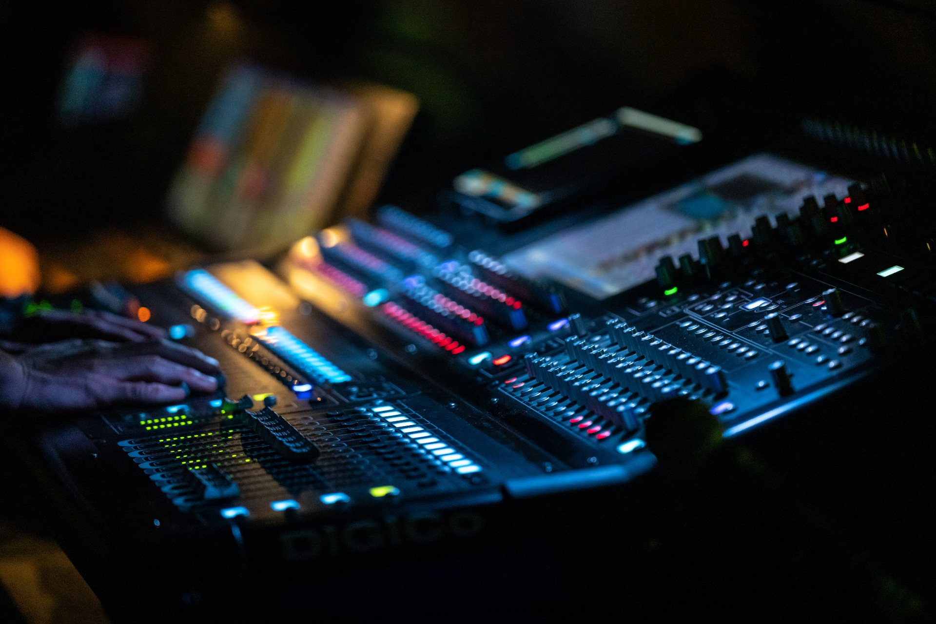 Hands adjusting a colorful audio mixing console in a dark studio
