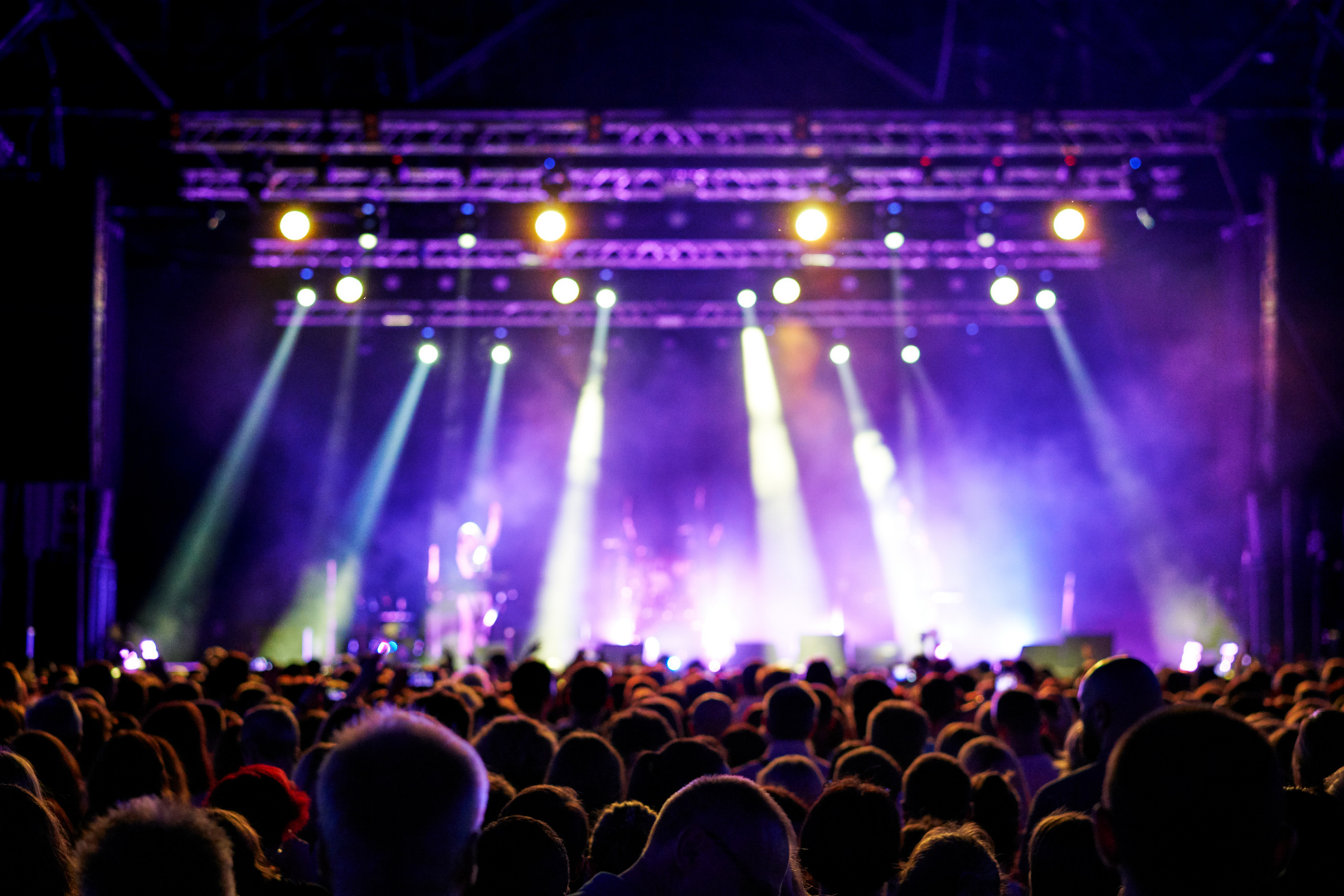 Concert stage with bright purple and white lights shining over a crowd at night