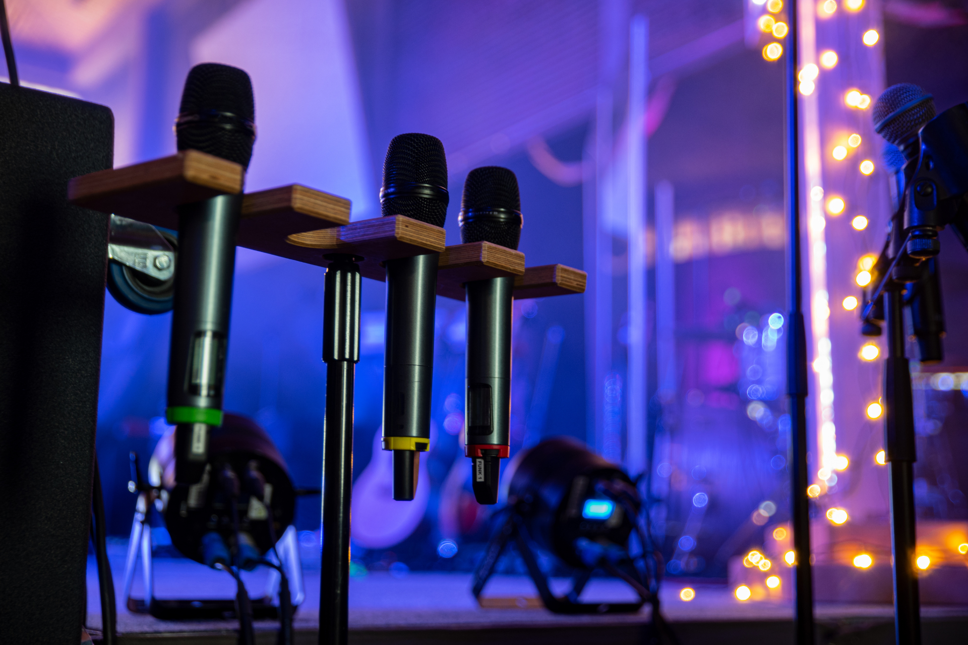 Three microphones on stands in a purple-blue lit studio with blurred stage lights in the background