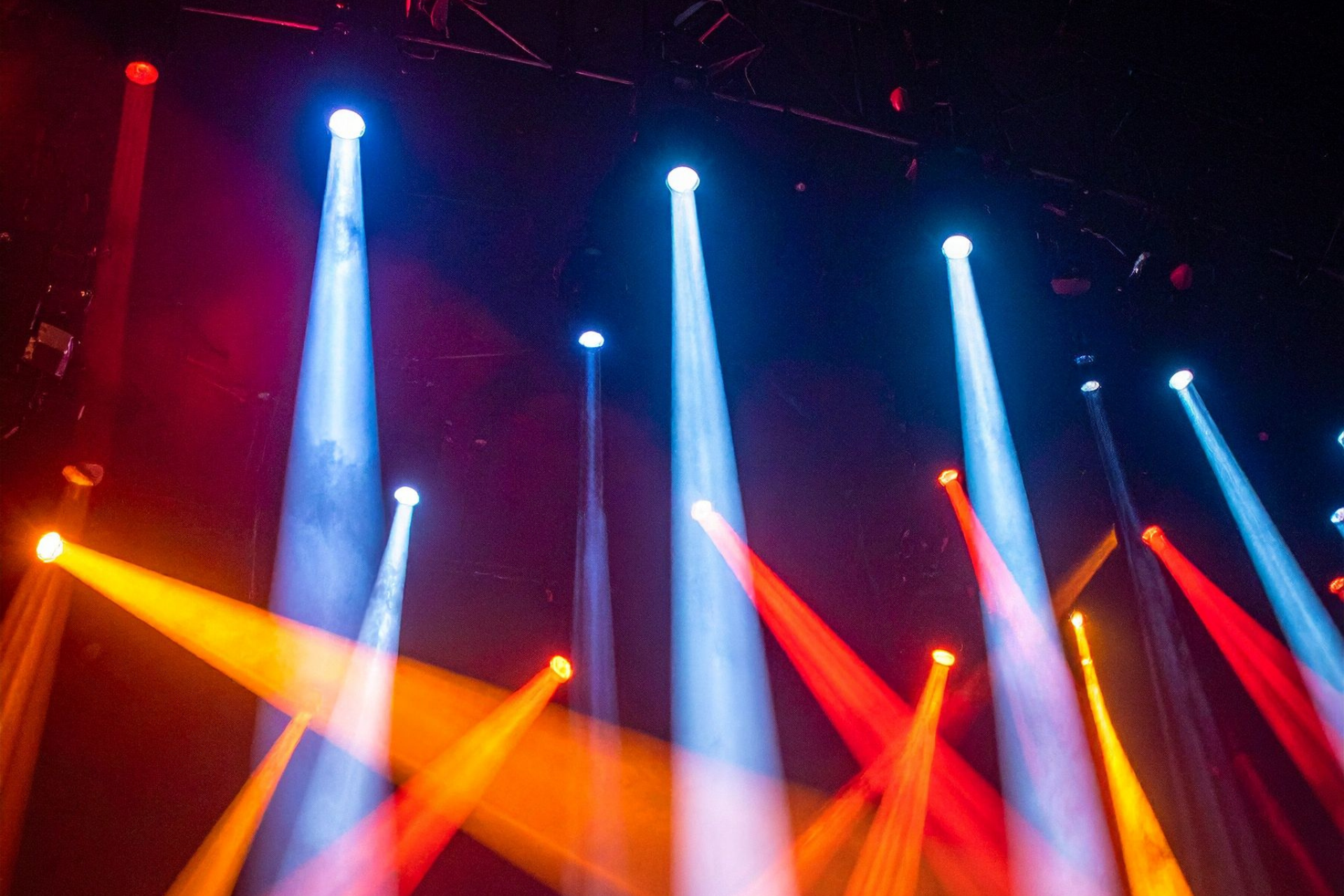 Colorful stage spotlights in blue, red, and orange beams against a dark concert background