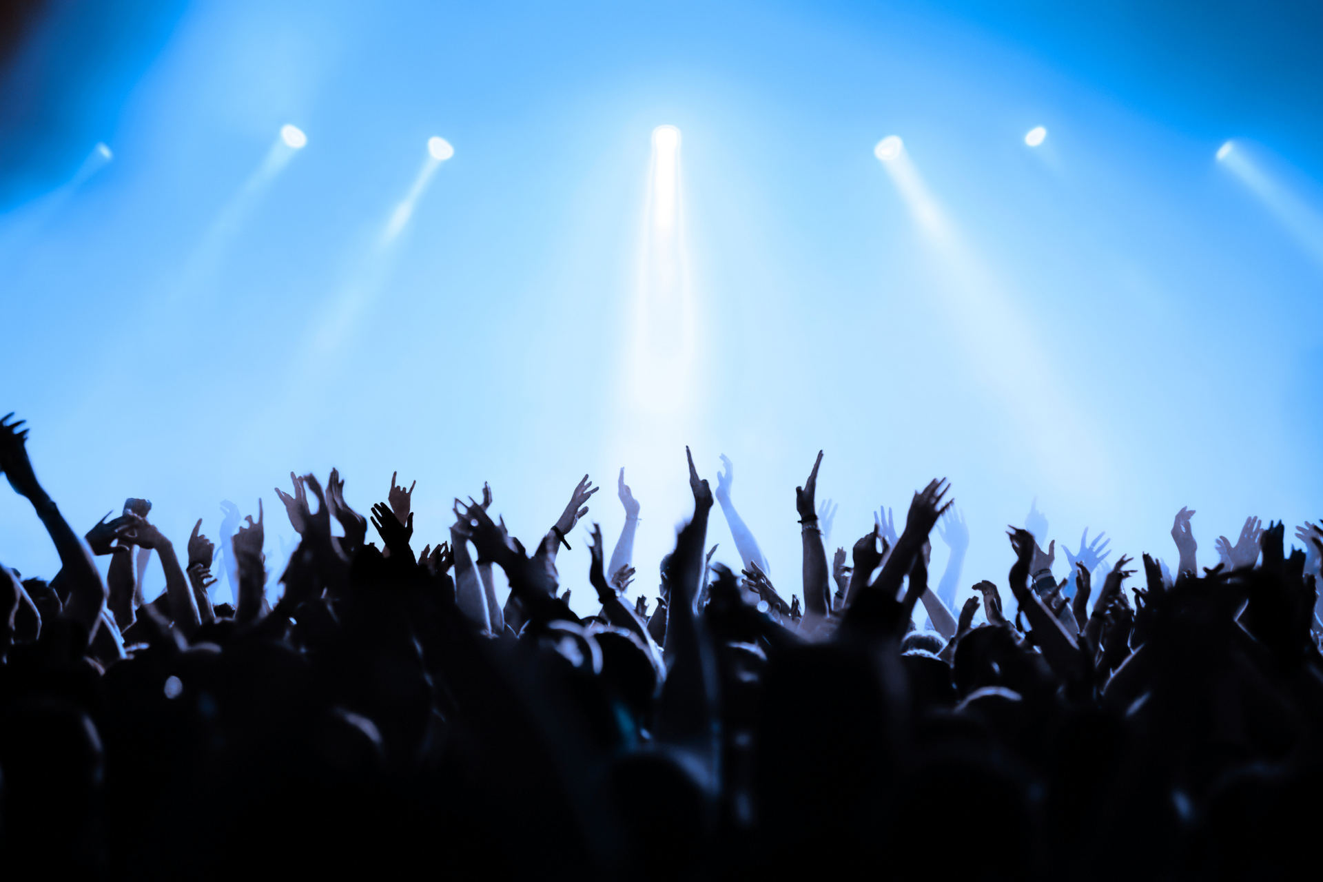 Silhouetted crowd cheering under blue stage lights at a concert