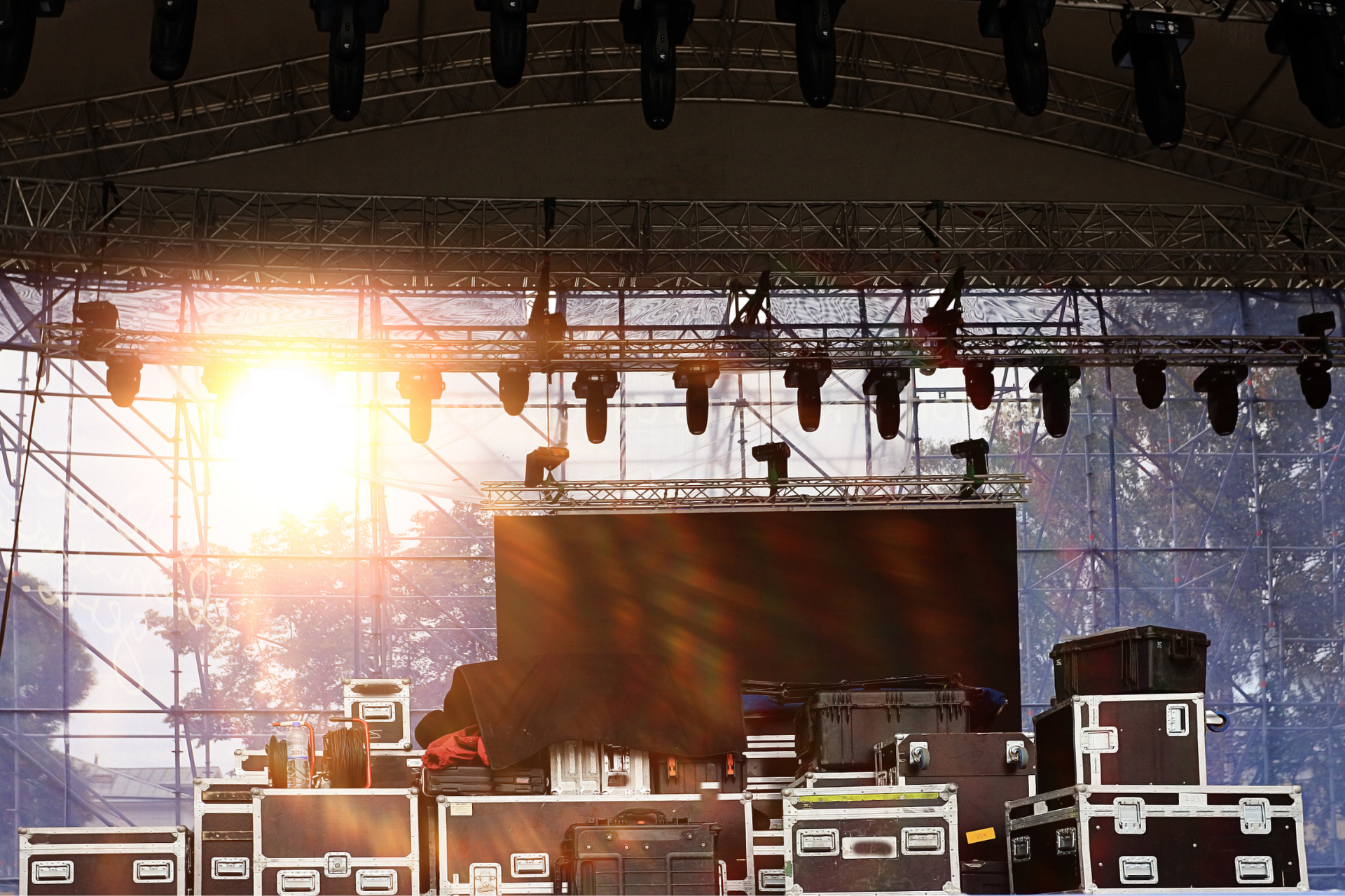 Outdoor concert stage at sunset with lighting rig and equipment cases in front of a large empty screen