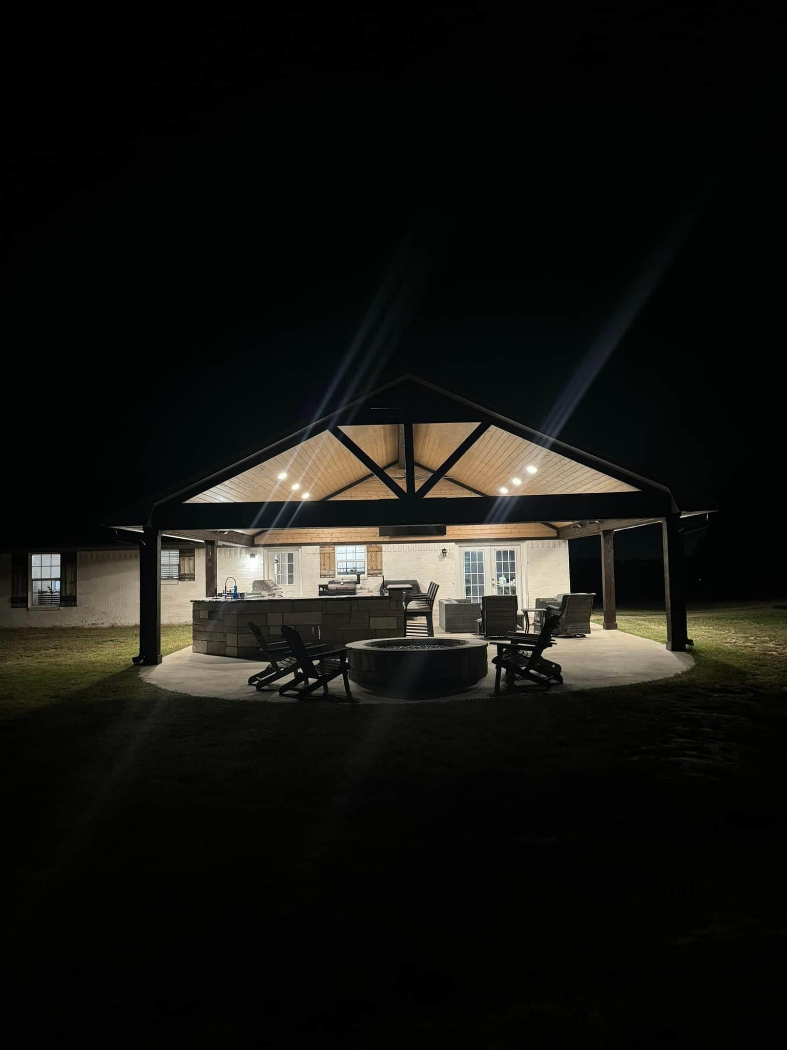 A house is lit up at night with a fire pit in front of it.