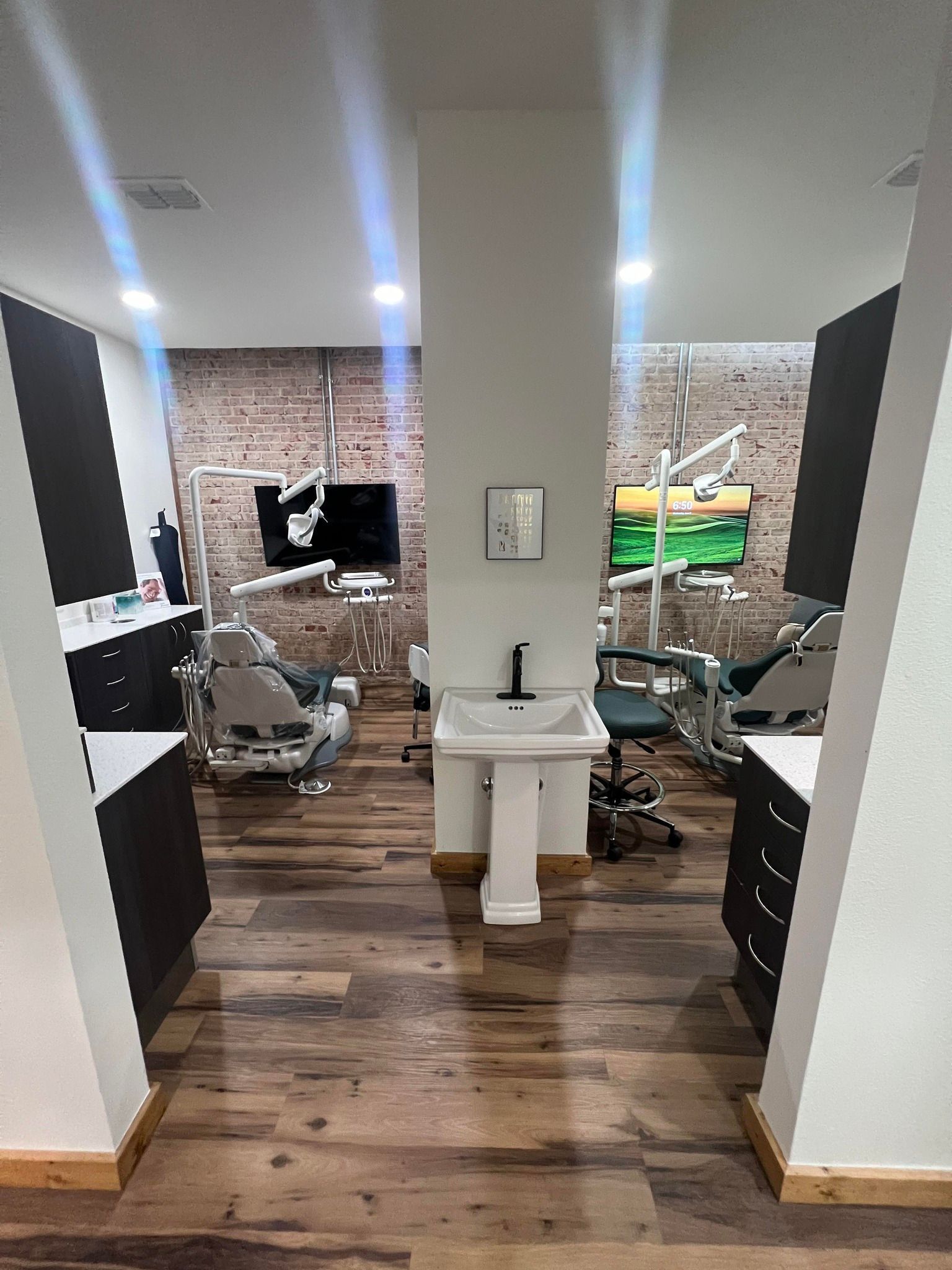 A dental office with a sink , chairs , and a brick wall.