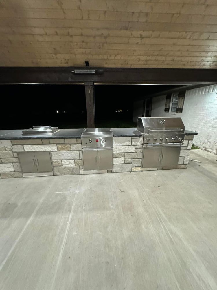A large outdoor kitchen with stainless steel appliances and a brick counter top.