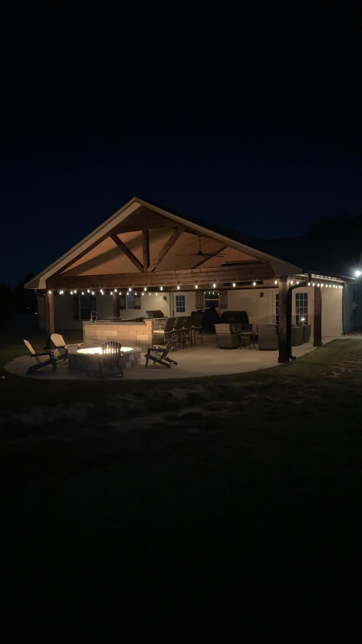 A large covered patio area with a fire pit in the middle of it at night.