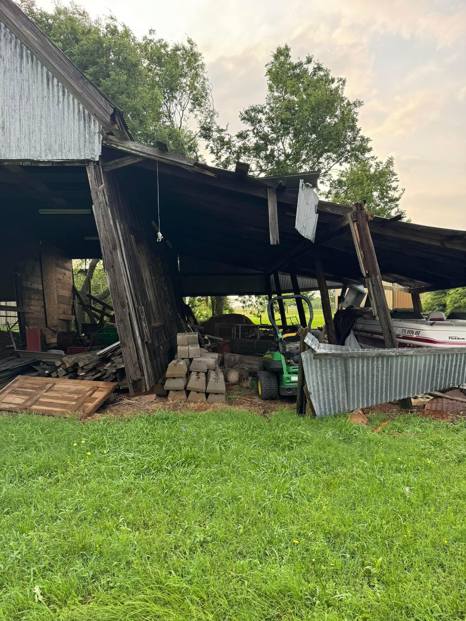 A barn with a broken roof is sitting in the middle of a lush green field.