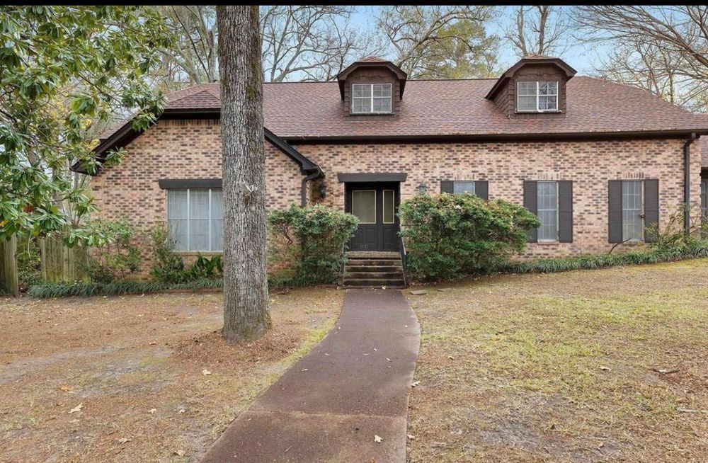 A brick house with a brown roof and black shutters is for sale.