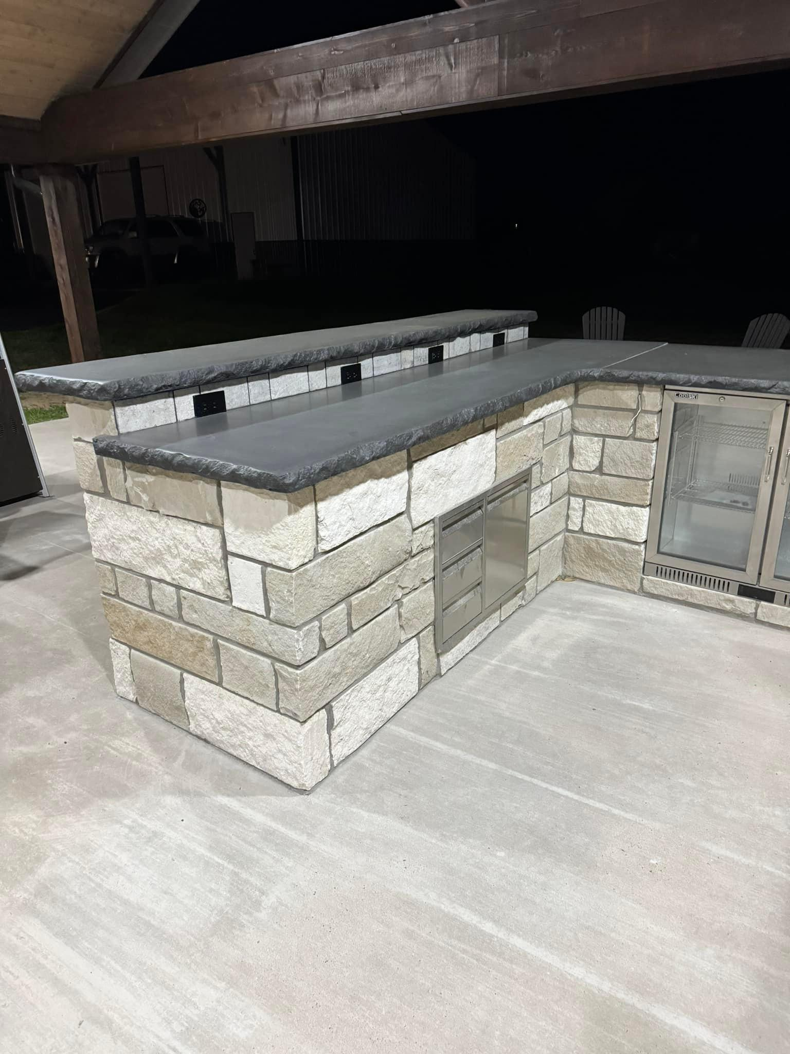 A kitchen island made of bricks and granite is sitting on top of a concrete floor.
