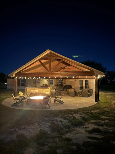 A pavilion with a fire pit and patio furniture underneath it at night.