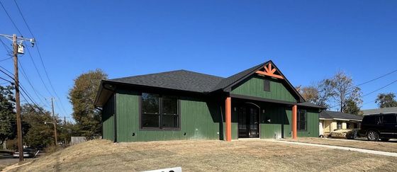 A green house with a black roof is sitting on top of a grassy hill.