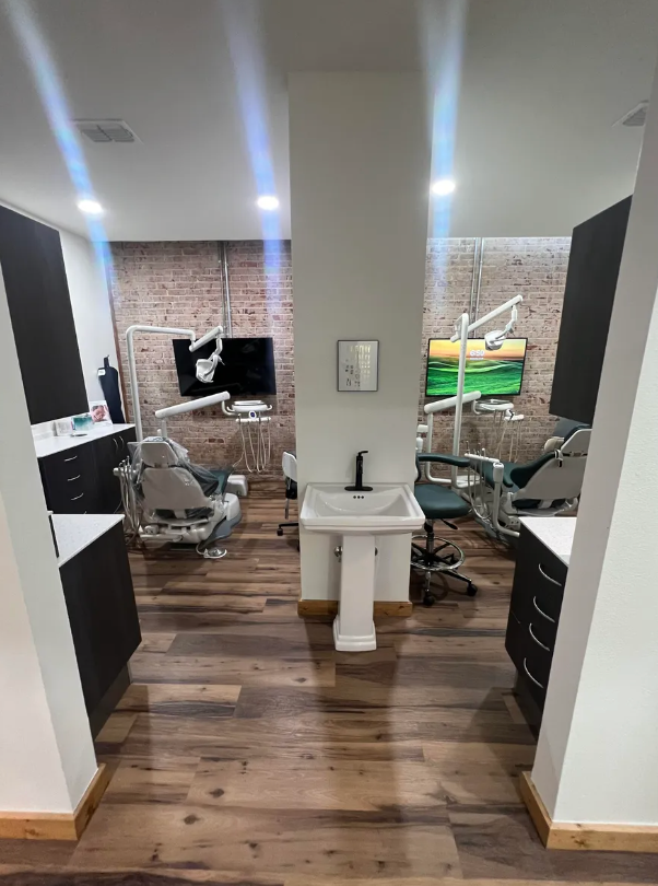 A dental office with a sink , chairs , and a brick wall.
