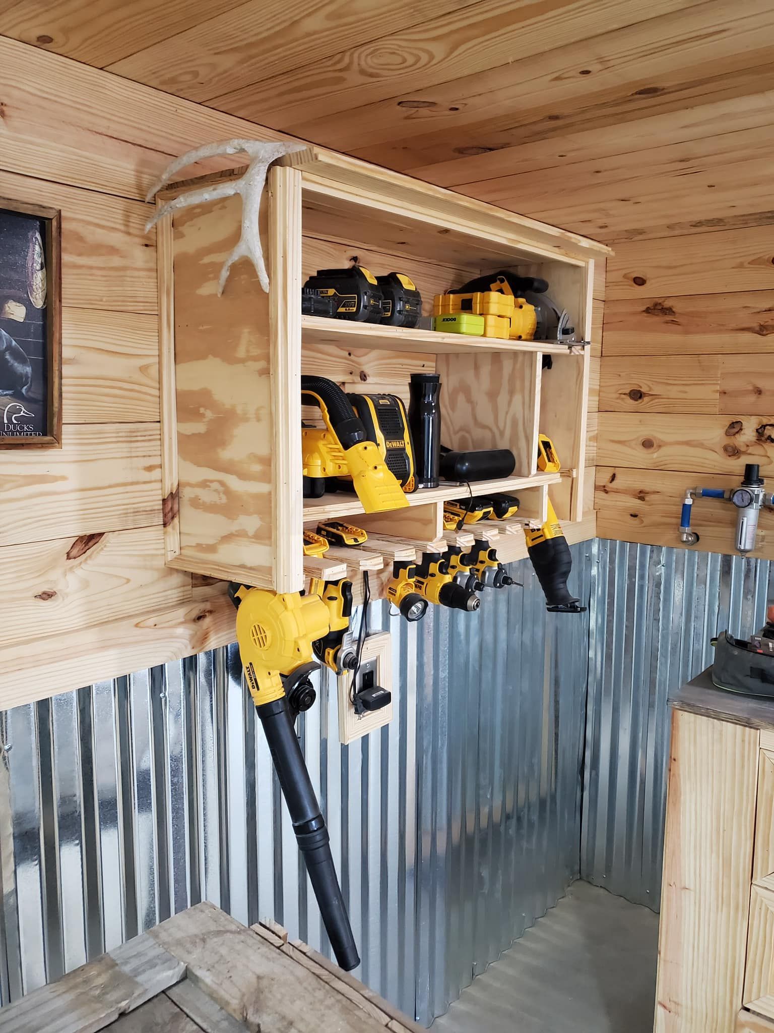 A wooden cabinet filled with tools is hanging on a wall in a garage.