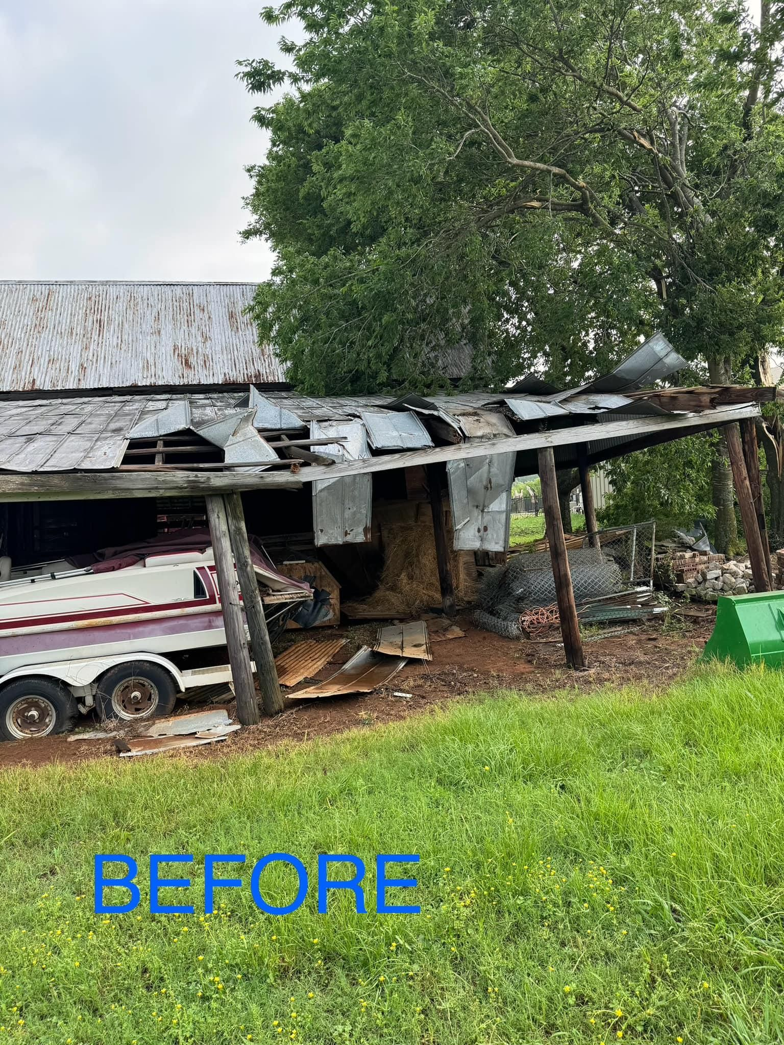 A boat is parked under a shed in a grassy field.