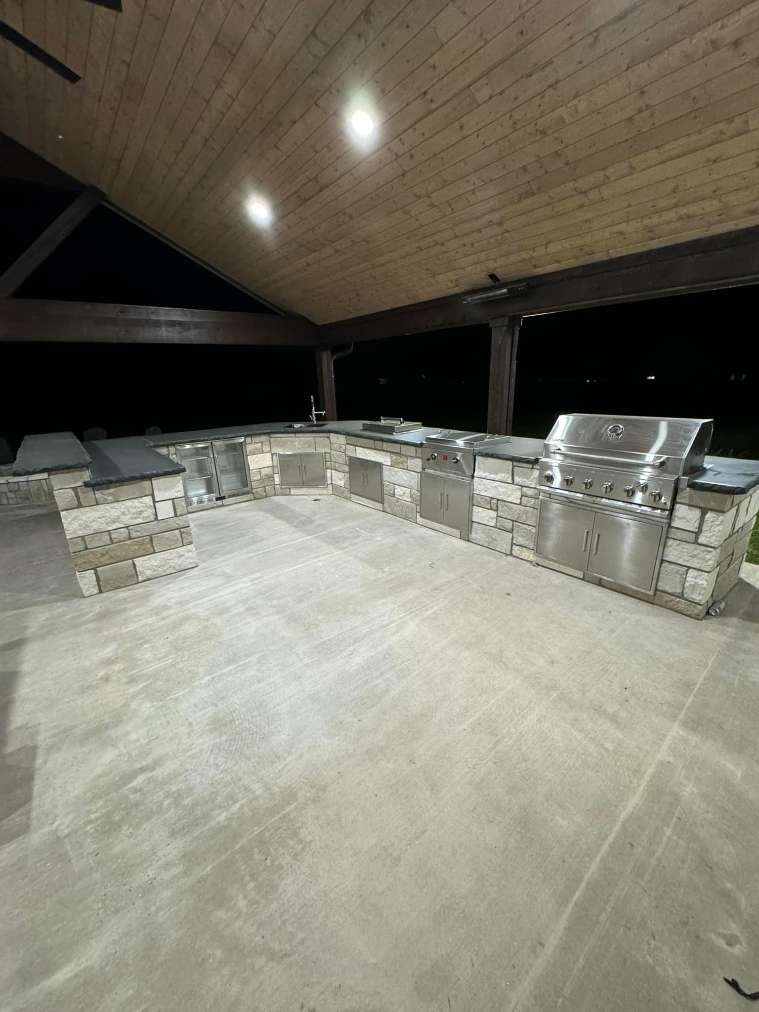 A large outdoor kitchen with stainless steel appliances and a wooden ceiling.