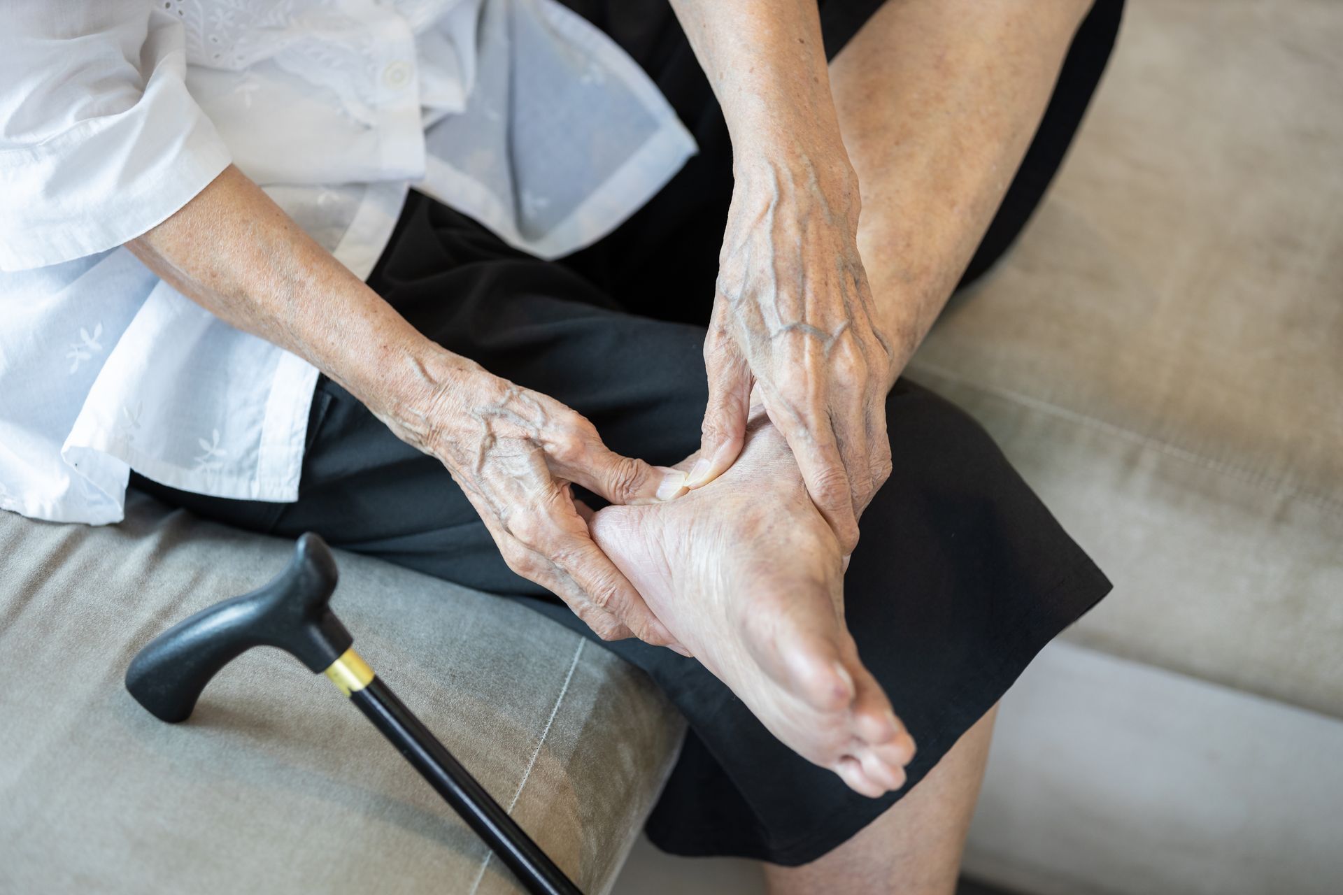 Elderly person holding foot, showing pain; cane nearby.