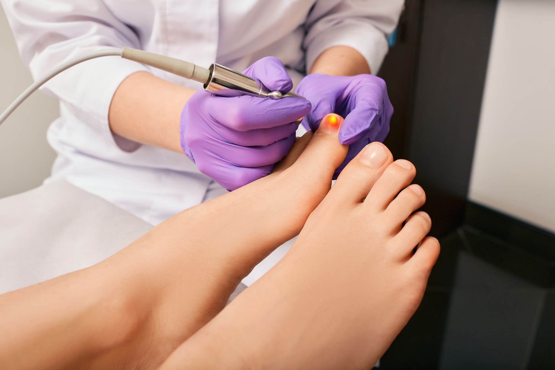 Person's feet getting a pedicure. Hands in purple gloves using a tool on a toe.