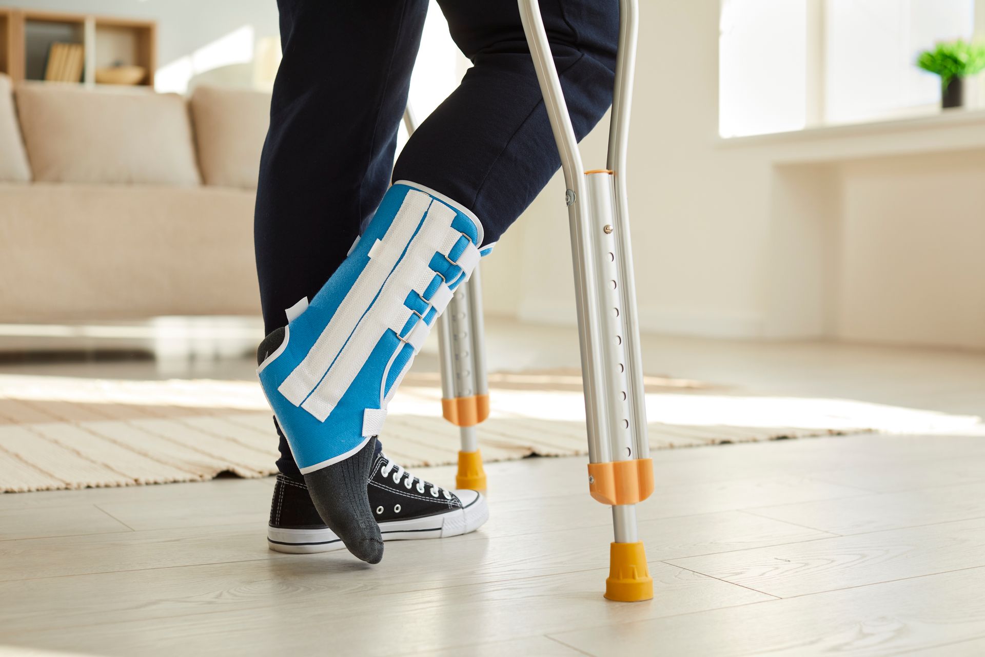 Person using crutches with a blue leg brace inside a home.