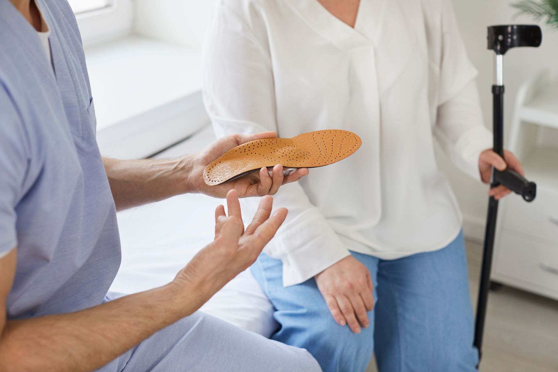 A healthcare worker shows an insole to a woman with a cane; indoor setting.