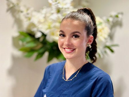 Eine Frau in einem blauen Kittel lächelt vor einer Vase mit Blumen.