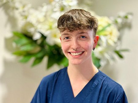 Eine junge Frau in einem blauen Kittel lächelt vor einer Vase mit Blumen.