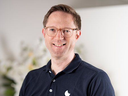 Ein Mann mit Brille und blauem Poloshirt lächelt in die Kamera.