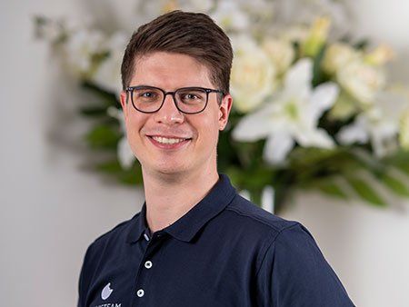Ein Mann mit Brille und blauem Hemd lächelt vor einer Blumenvase.