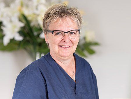 Eine Frau mit Brille und blauem Kittel lächelt in die Kamera.