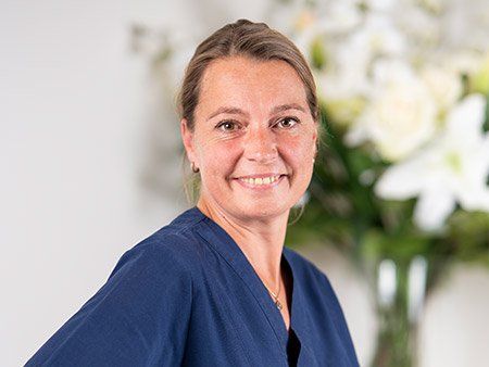 Eine Frau in einem blauen Kittel lächelt vor einer Vase mit Blumen.