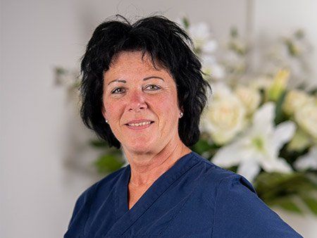 Eine Frau in einem blauen Kasack steht vor einer Vase mit Blumen.