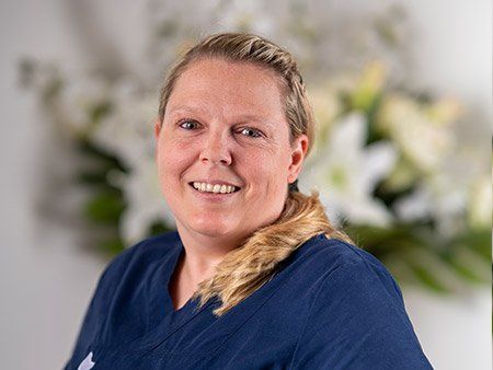 Eine Frau in einem blauen Kittel lächelt vor Blumen.