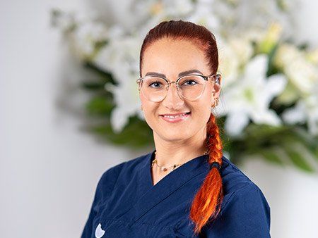 Eine Frau mit Brille und blauem Kittel steht vor einem Strauß weißer Blumen.