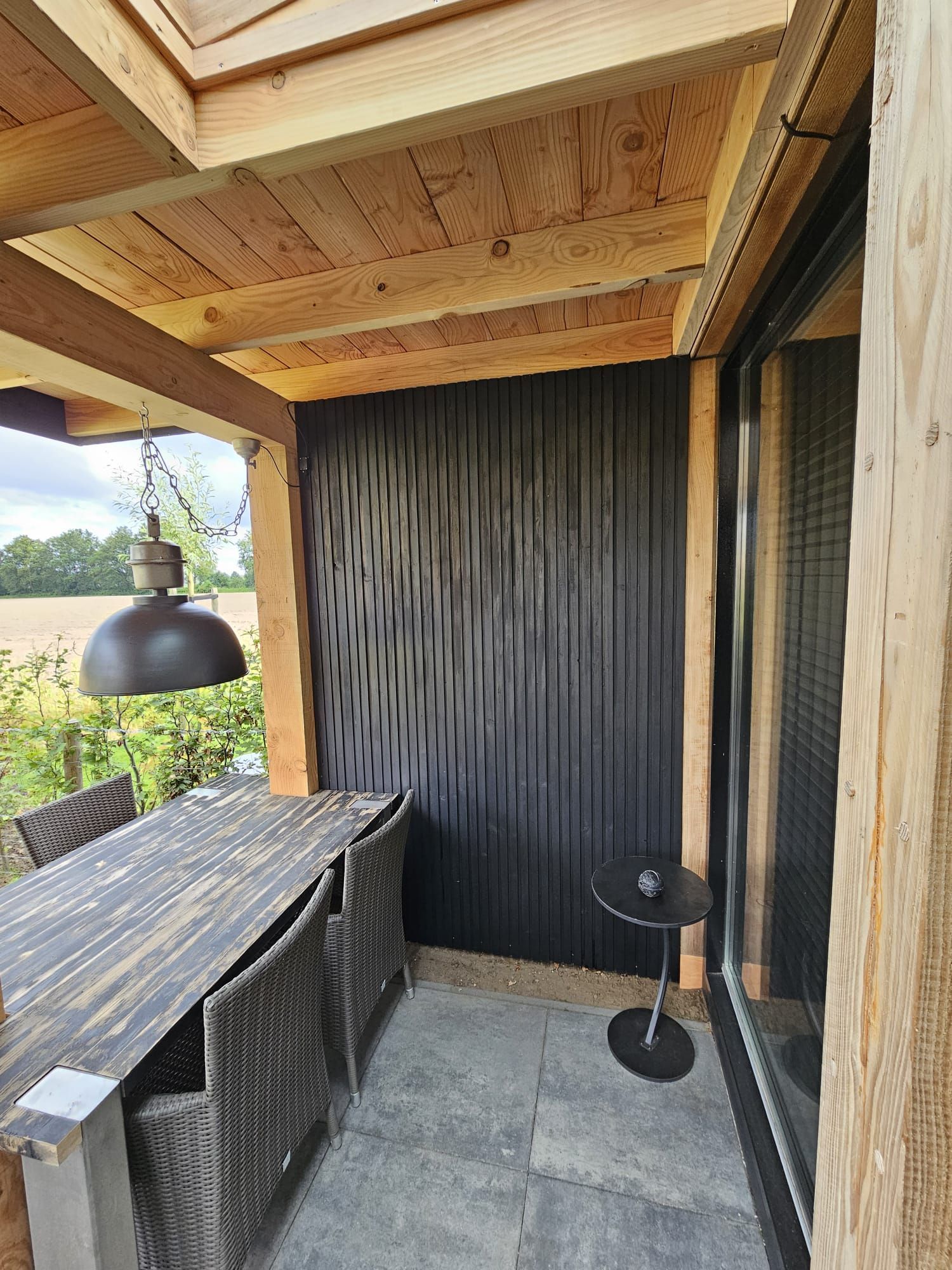 Een terras met een tafel en stoelen onder een houten dak.