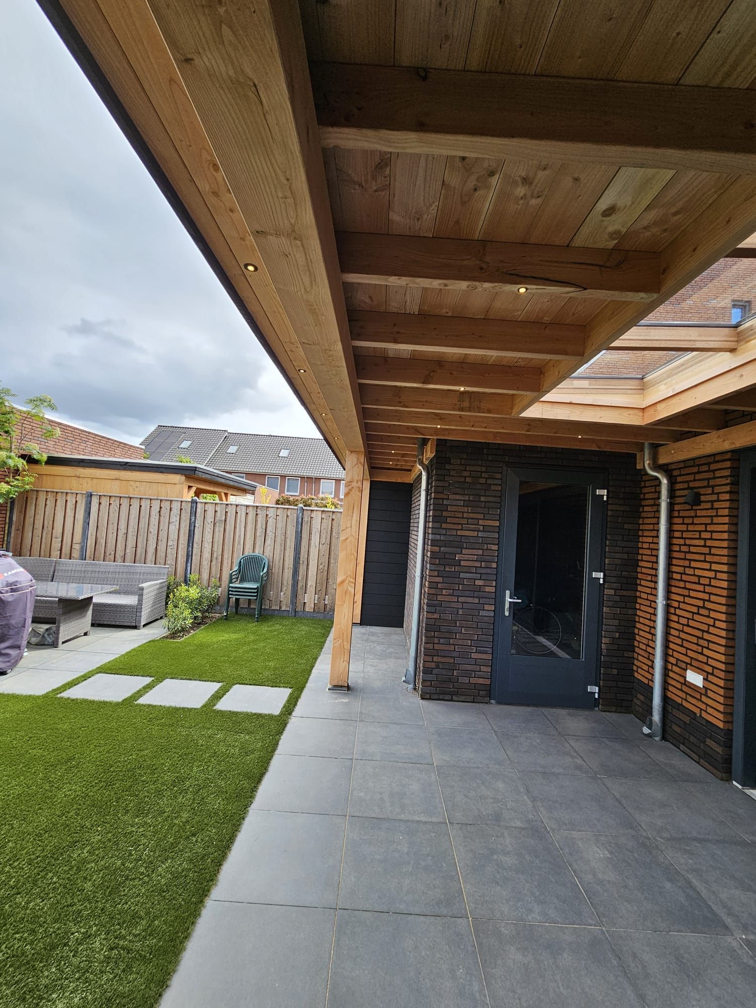 Een veranda met een houten dak dakbeschot en lichtstraat.