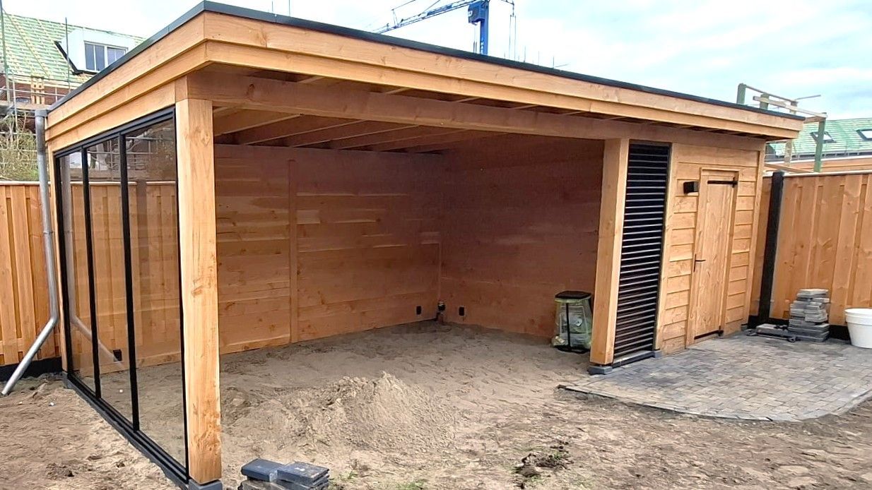 Houten schuur met glazen panelen en een grindvloer, gebouwd in een tuin.