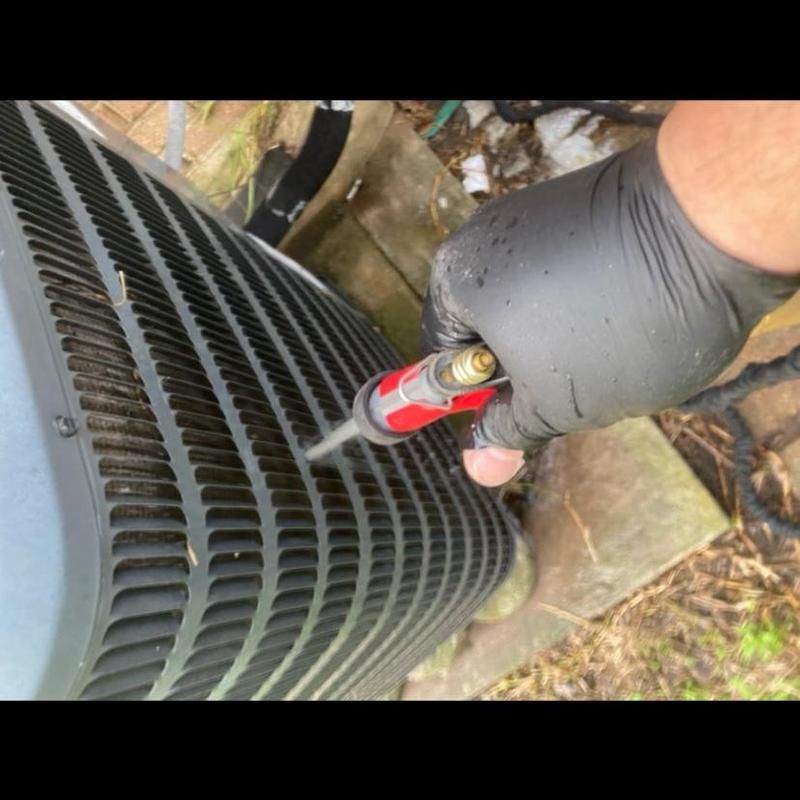 Person in black glove using tool on an air conditioning unit outside.