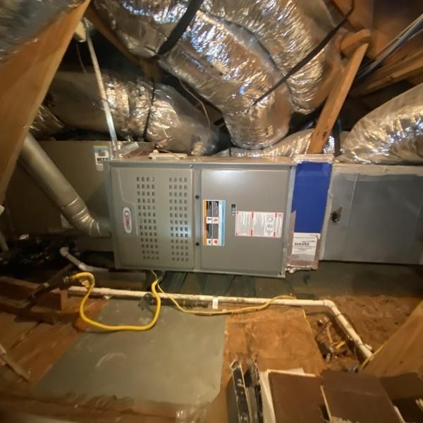 HVAC unit in an attic with ductwork. Gray unit with blue filter. Yellow wire and exposed wood.