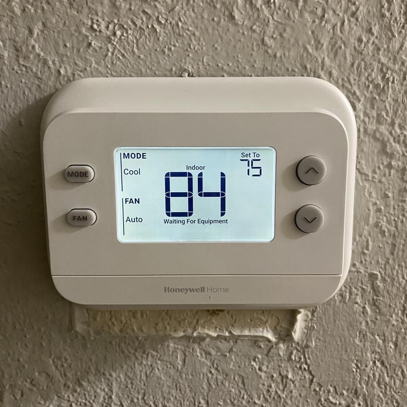 White Honeywell thermostat on a textured wall, , with mode selections and up/down buttons.