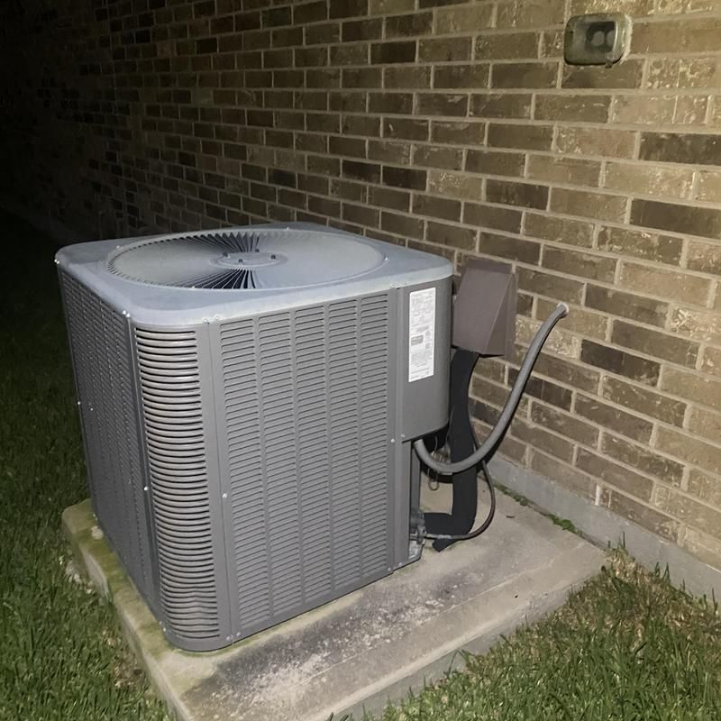Gray air conditioning unit next to a brick wall, at night.