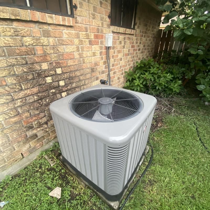Air conditioning unit next to brick building, with a green yard.