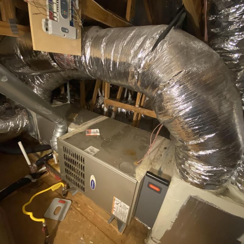 HVAC unit in attic with silver ductwork, electrical components, and wooden rafters.