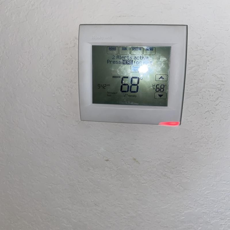 White thermostat on a wall, displaying a temperature of 68 degrees. A red light is on.