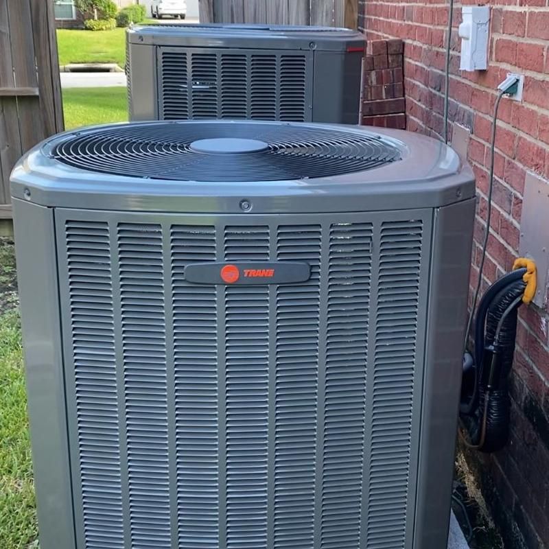 Two gray Trane air conditioning units outside a brick building.