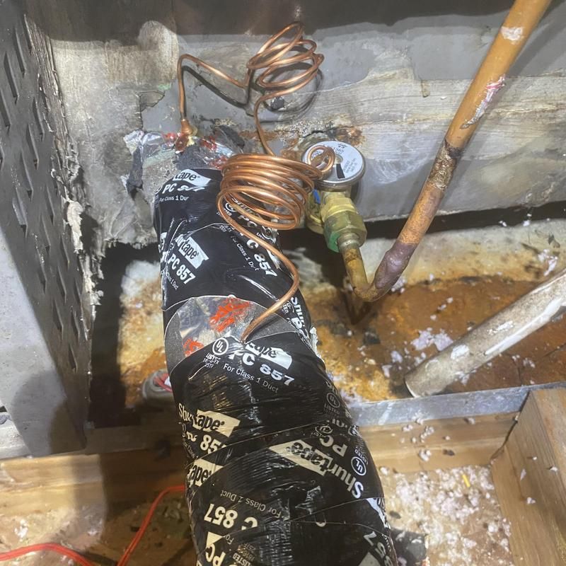 Damaged HVAC unit with exposed copper pipes and insulation in a damp, dirty enclosure.