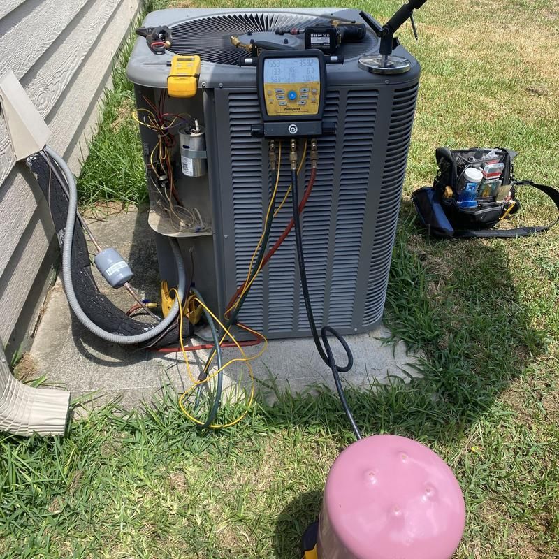 HVAC technician working on an outdoor AC unit. A pink tank and gauges connected with tubes.