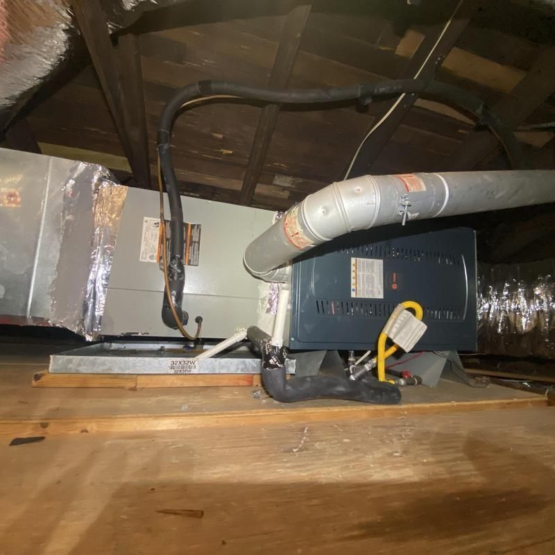 HVAC unit in an attic, featuring a silver air handler, ductwork, and a gray furnace.