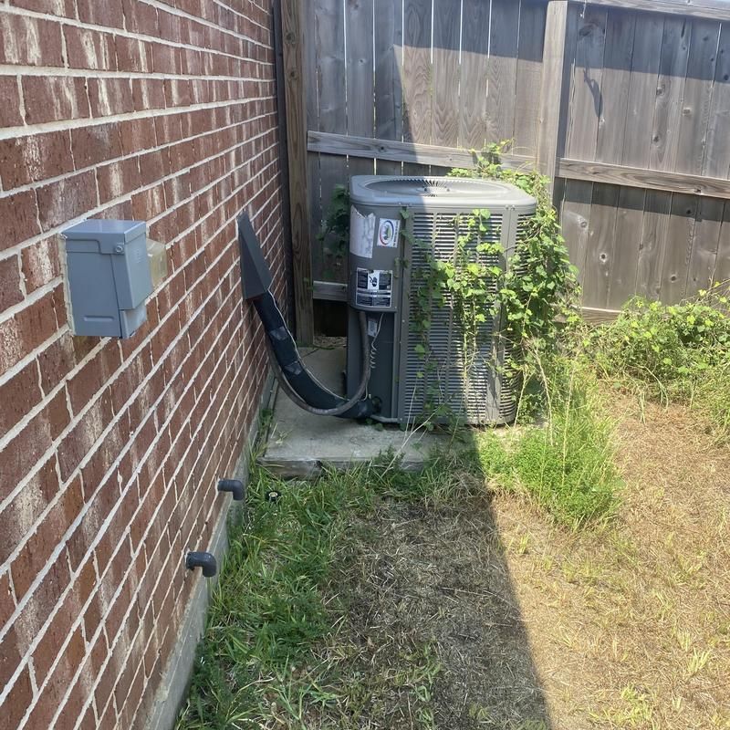 AC unit against a brick wall, overgrown with vines, next to a wooden fence.